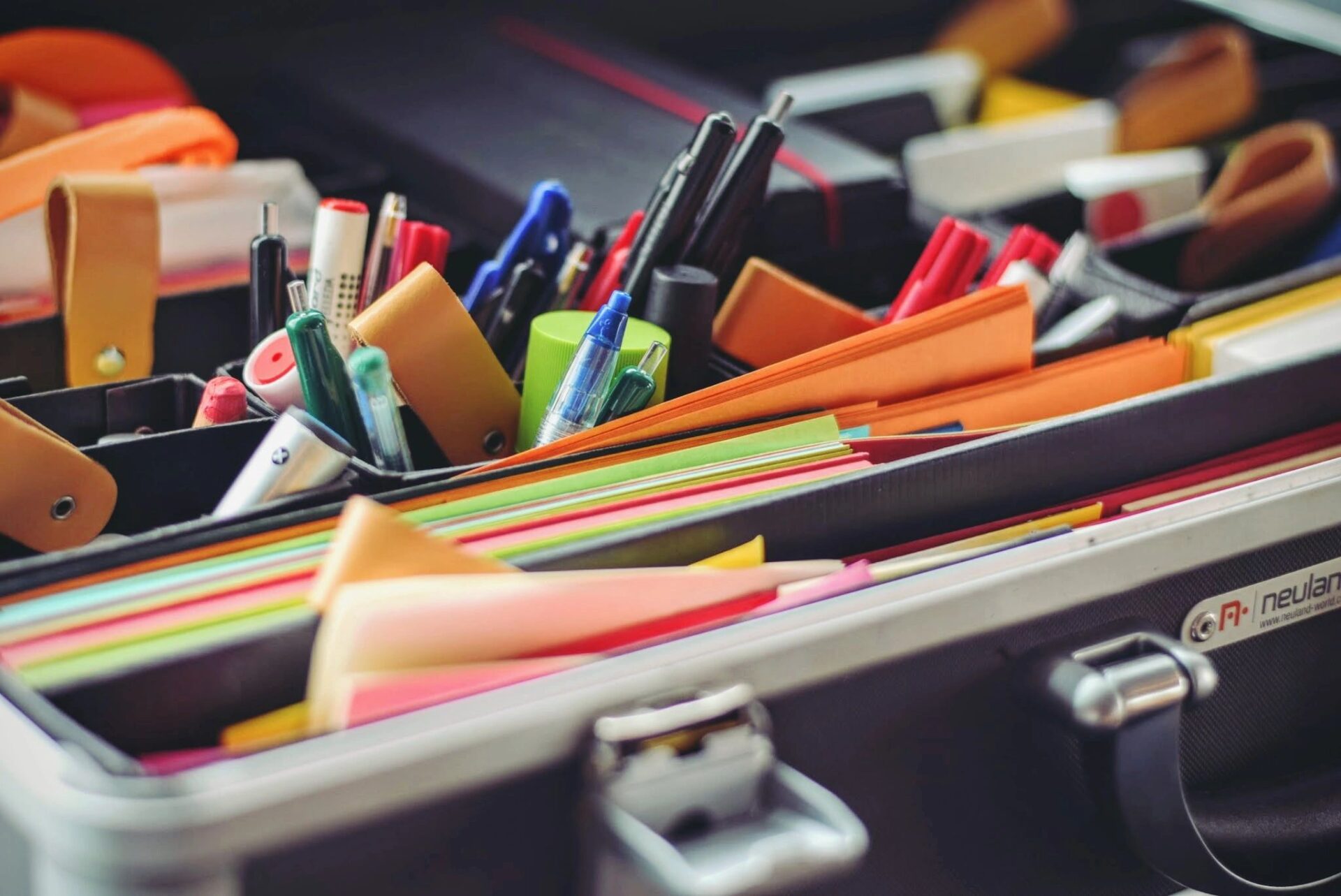 Assortment of colorful pens, folders, and notebooks in an open briefcase