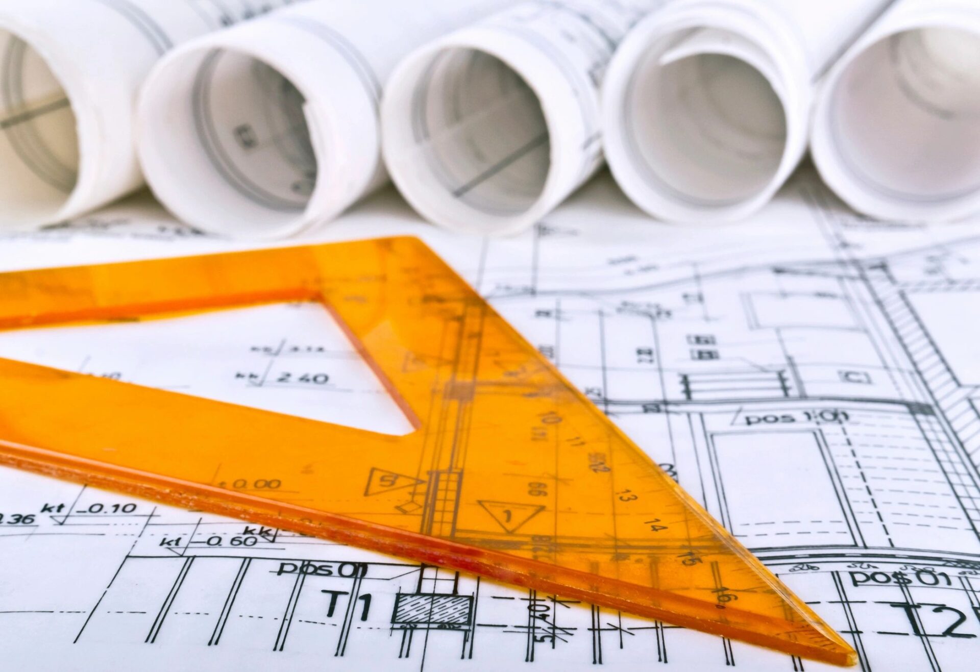 Rolled architectural blueprints and a translucent orange triangle ruler on top of technical drawings.