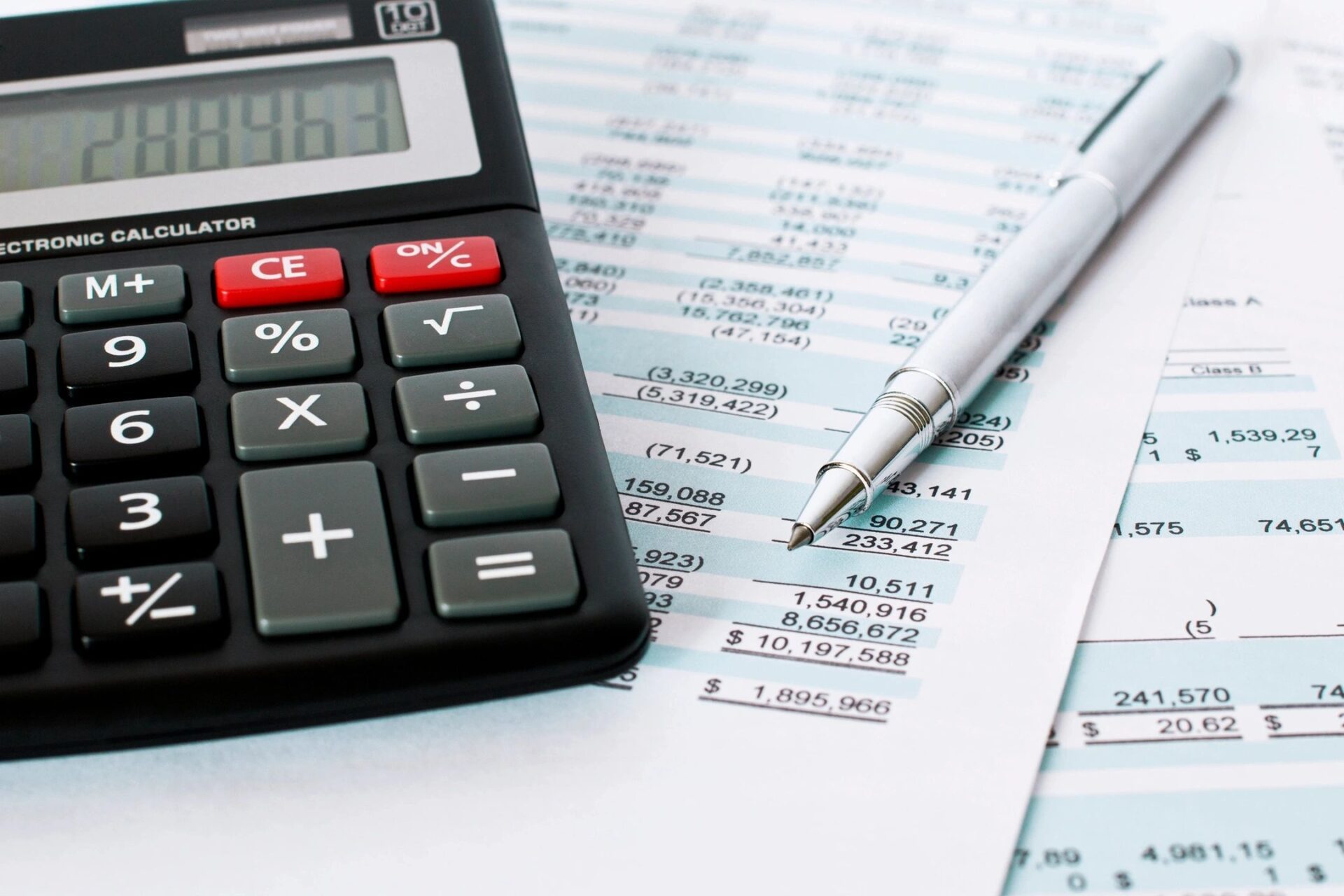 Financial documents with a calculator and metallic pen resting on spreadsheets filled with numerical data and account information.